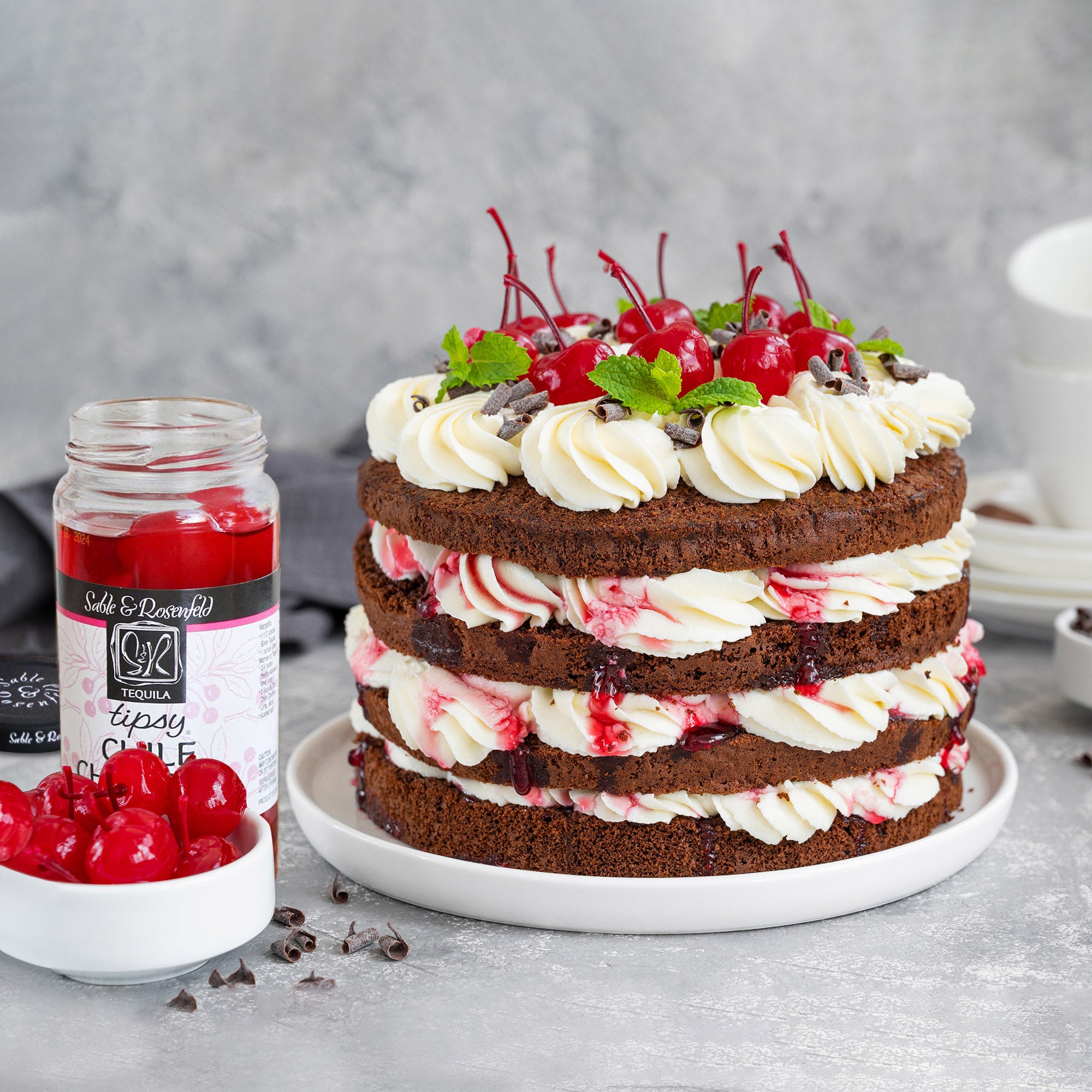 A decadent chocolate cake layered with cherry filling and whipped cream, topped with tequila-spiked maraschino cherries for a sweet indulgence.