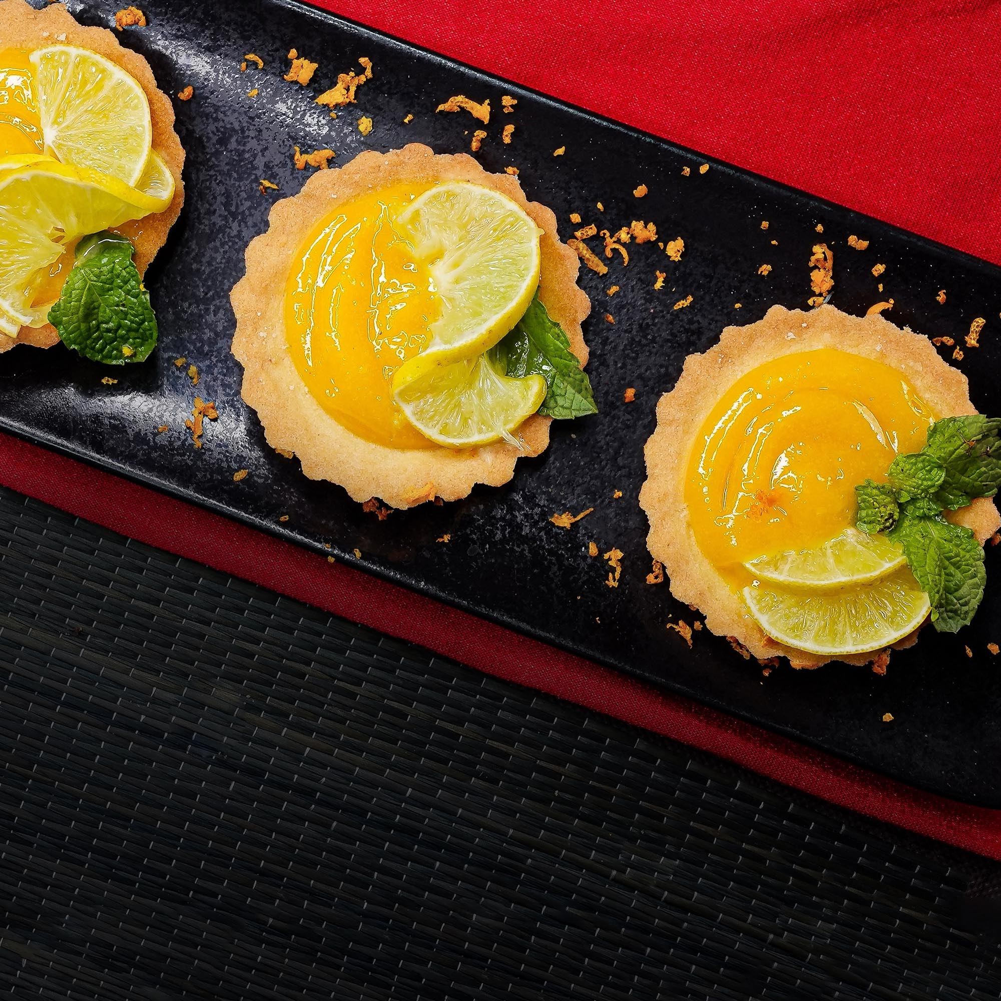 A black plate with three small tarts, topped with lime slices and mint, offering a delightful sweet treat for any event.