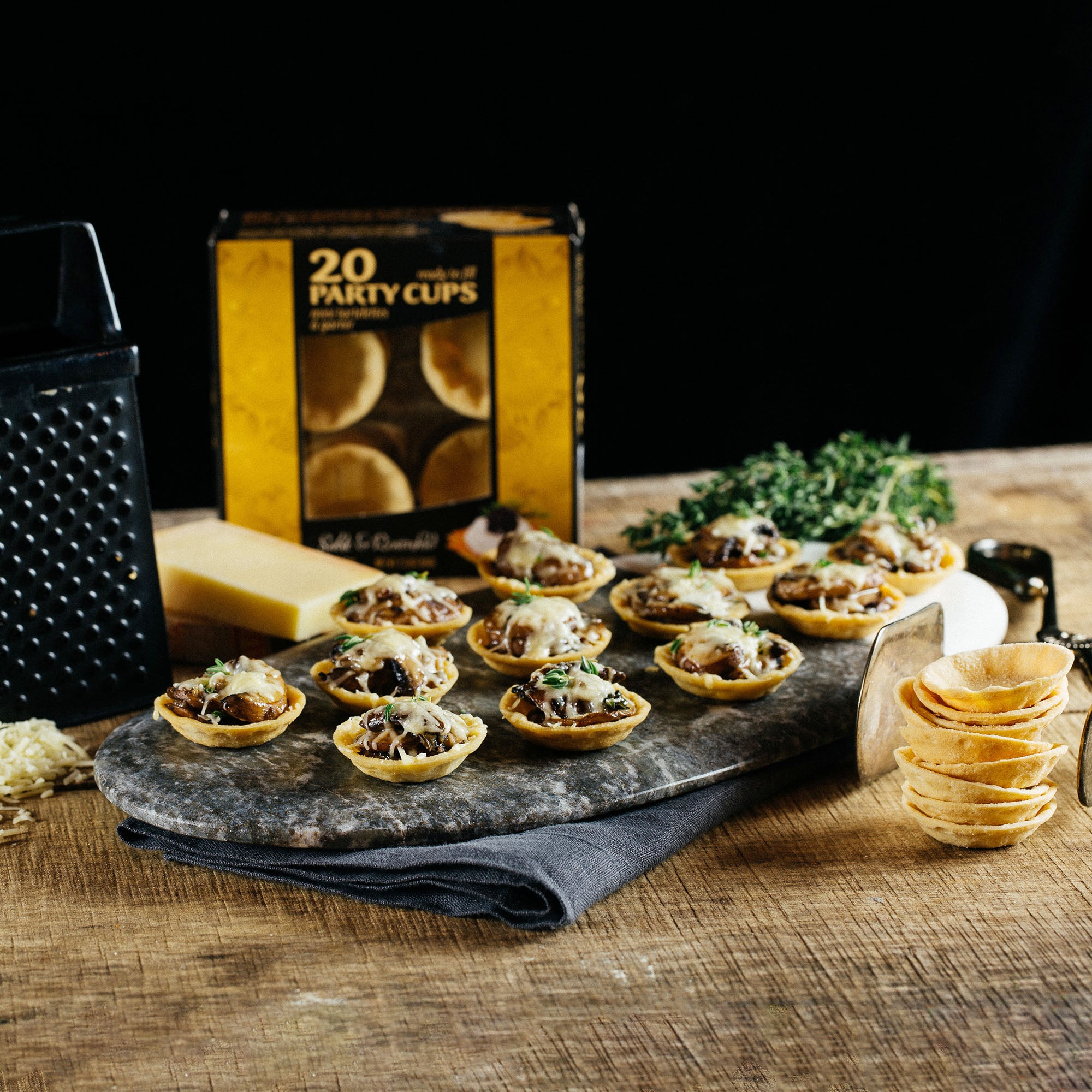 A wooden table displays a tray of all-natural Party Cups filled with savory ingredients, showcasing easy entertaining options.