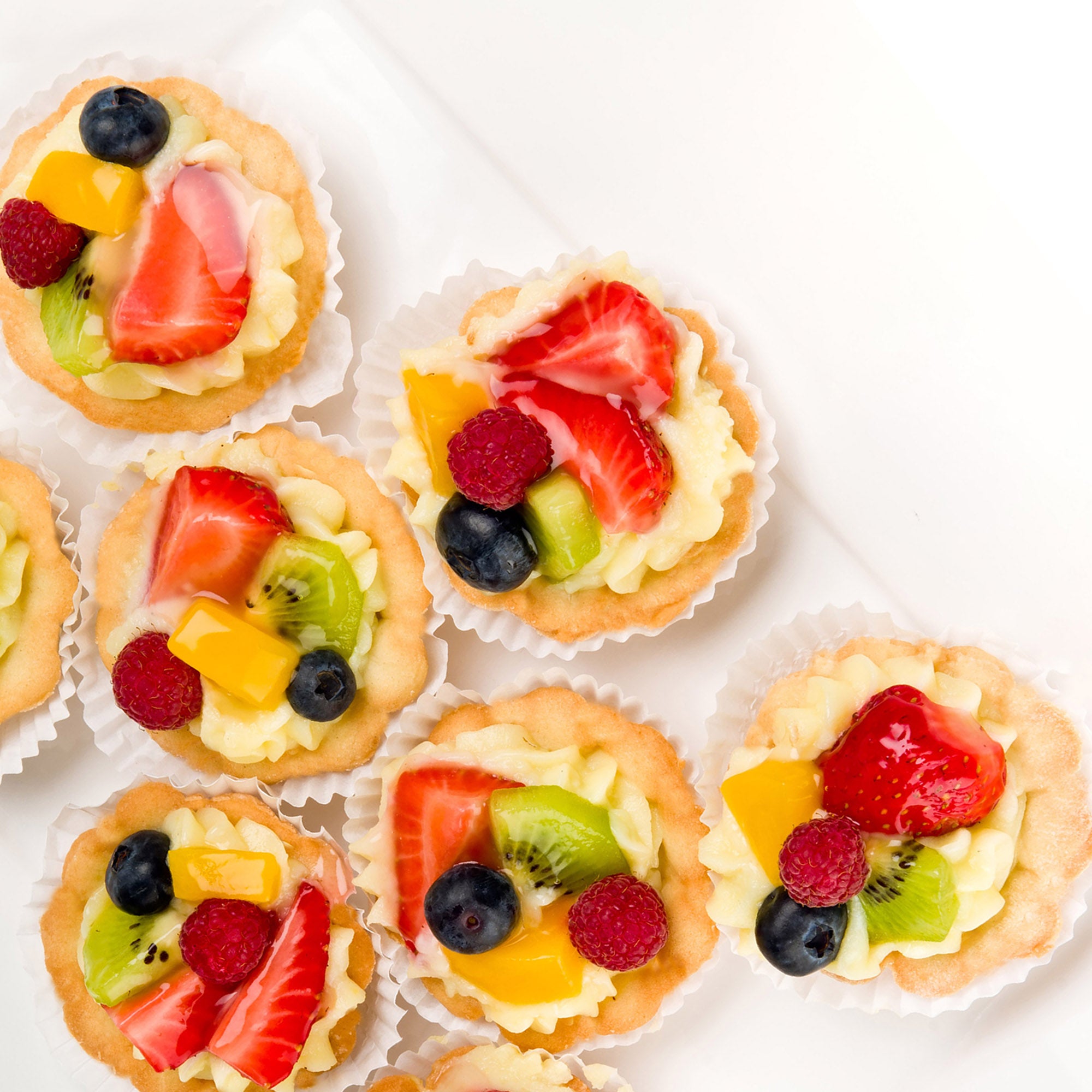 A white plate adorned with small fruit tarts, showcasing a delightful array of colors and textures for any gathering.