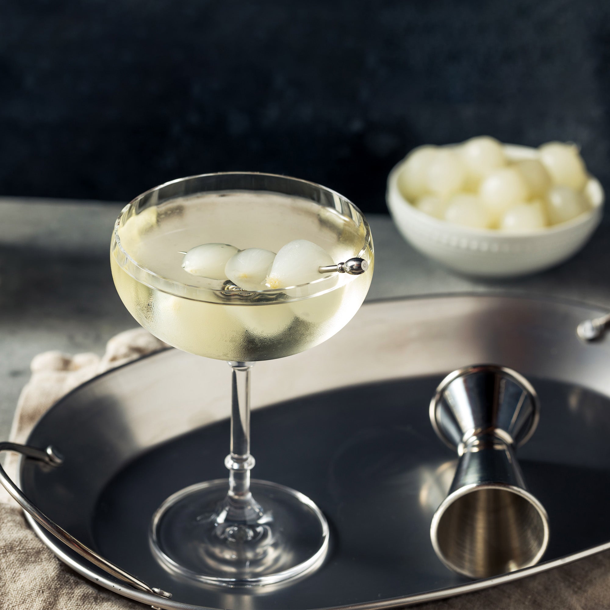 A martini glass garnished with Vermouth Tipsy Onions, displayed on a silver tray, offering a refined cocktail presentation.