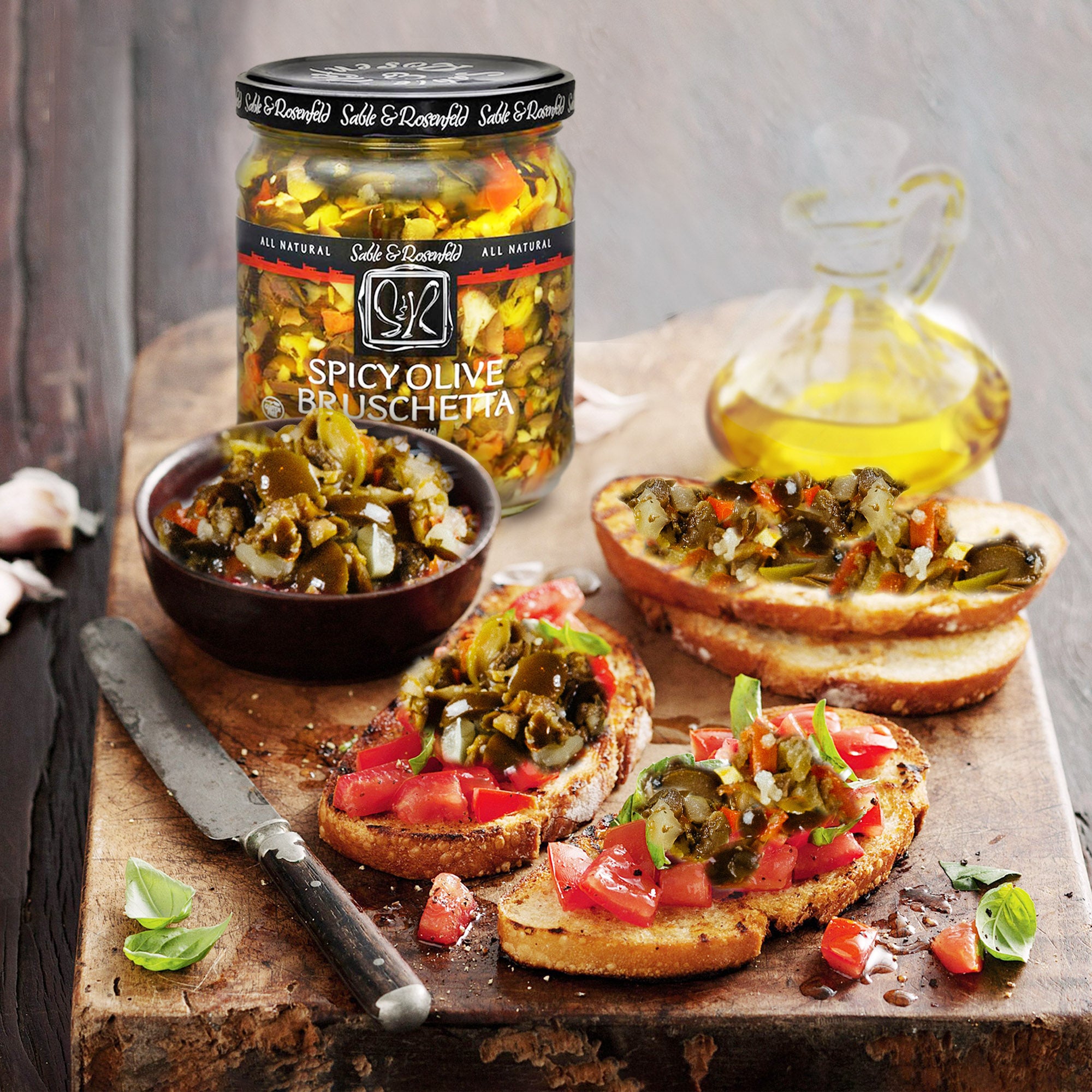 A rustic wooden board displaying toasted bread slices topped with Sable & Rosenfeld Spicy Olive Bruschetta, accompanied by a bowl of the bruschetta mix, fresh basil leaves, and a bottle of olive oil, creating a vibrant and flavorful appetizer spread.