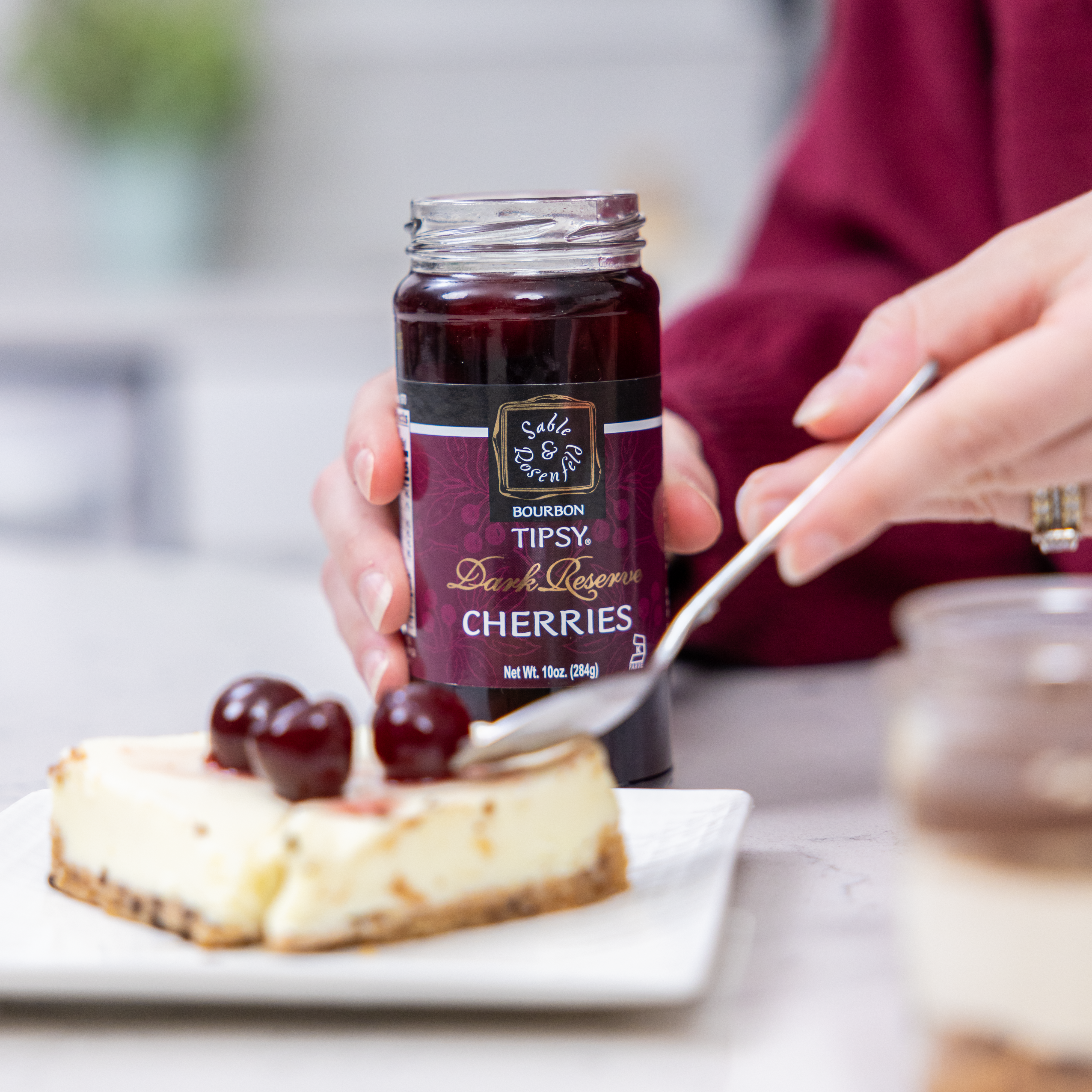 Jar of bourbon infused cherries by Sable & Rosenfeld with a cheesecake dessert