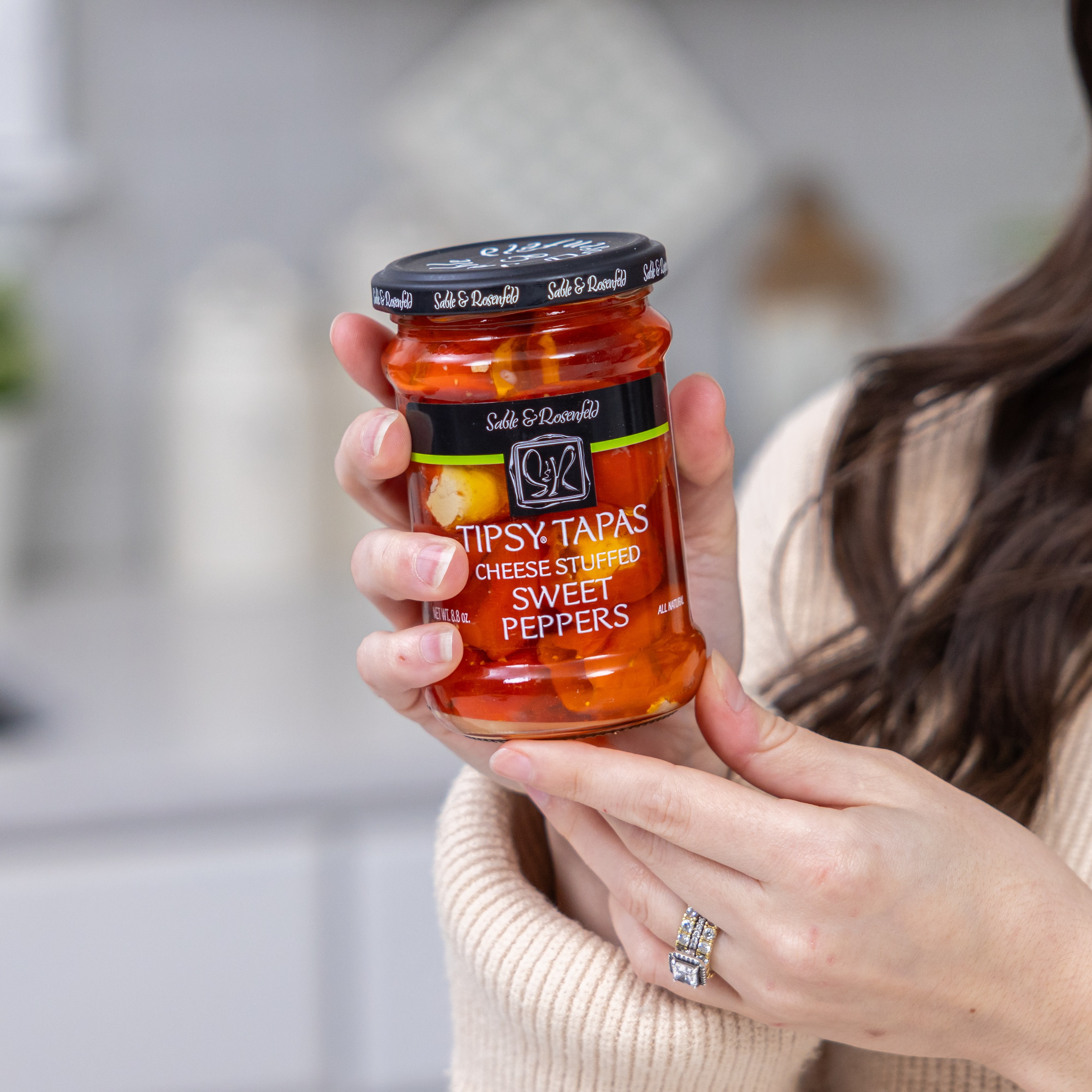 Jar of cream cheese stuffed mini sweet peppers held by a woman in a cozy setting, featuring gourmet appetizers perfect for entertaining.