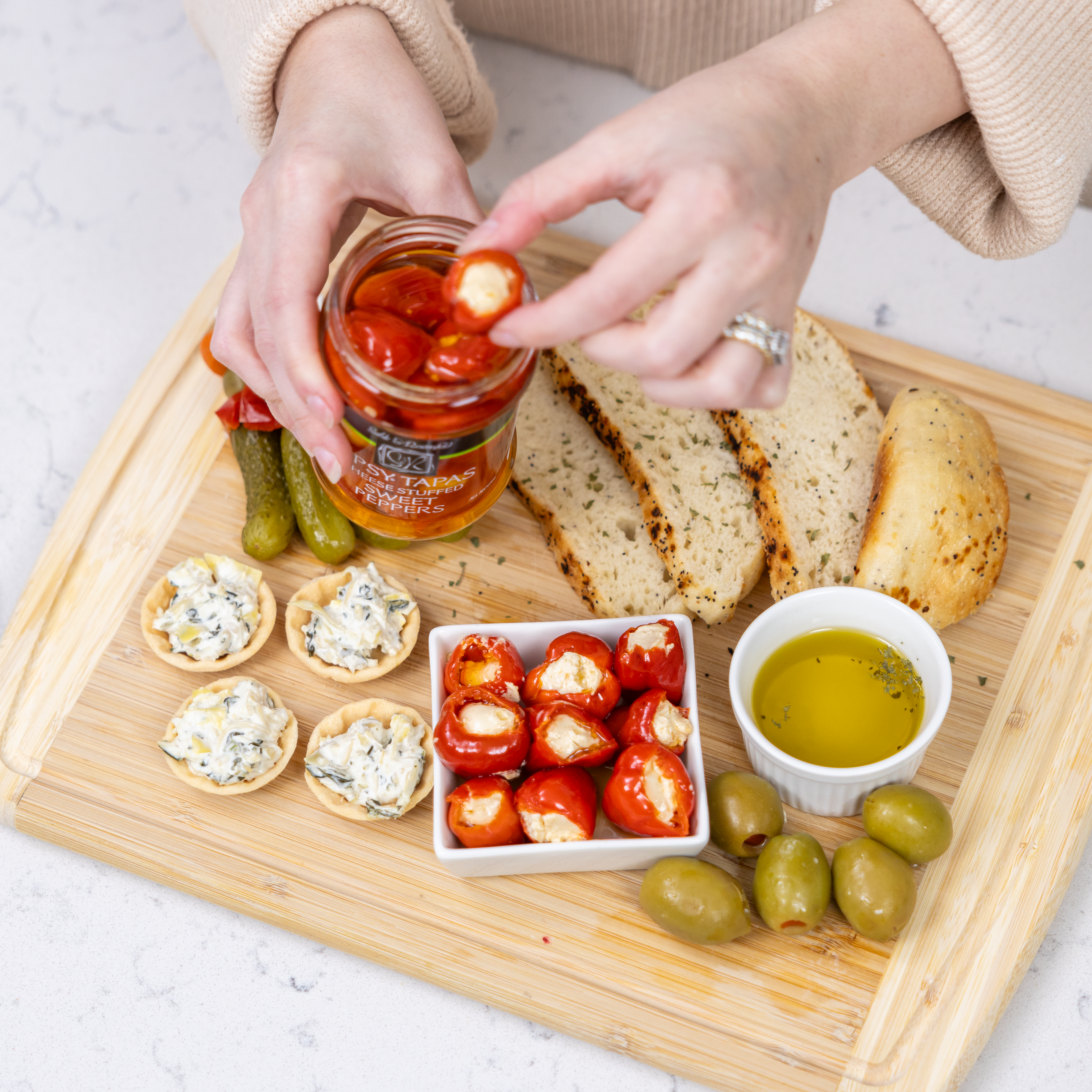 Modern gourmet foods platter featuring cheese-stuffed sweet peppers, olives, artisan bread, and a jar of gourmet appetizers for an elegant dining experience.