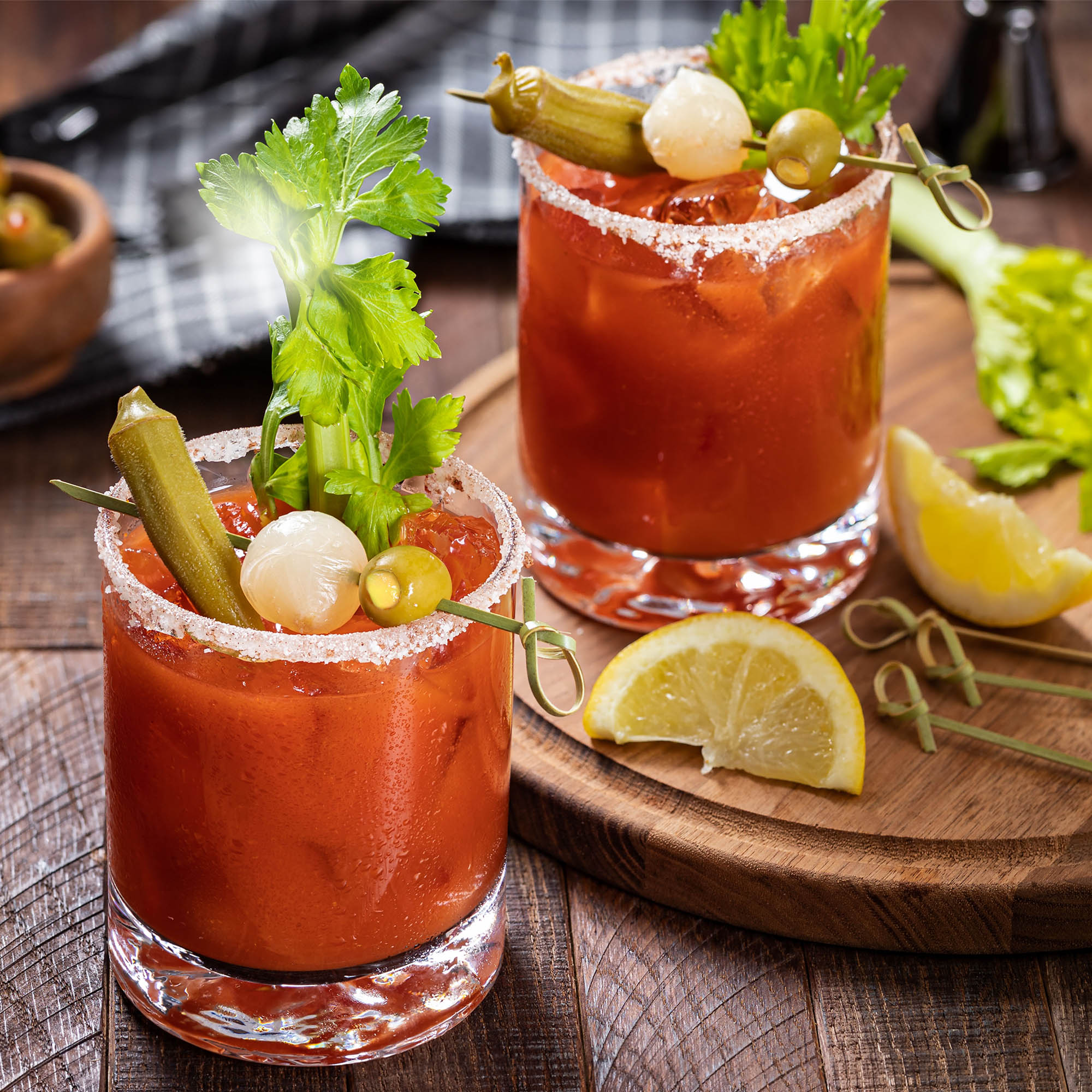 Two glasses filled with a vibrant bloody drink, garnished with lemon and gin-soaked olives, showcasing a refreshing cocktail experience.